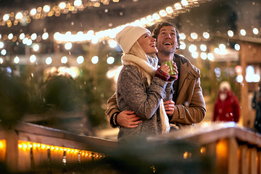 Joyful couple looking at Christmas lights. Winter village setting.